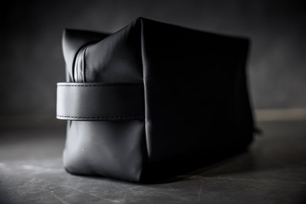 Musta KOMEA toilettilaukku sivusta kuvattuna, näkyvissä kantolenkki